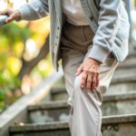 膝をさすりながらゆっくりと慎重に階段を降りる高齢者  膝の痛みとシニアライフのイメージ