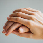 A high-quality close-up of hands gently protecting and covering another hand, creating a powerful symbol of trust, care, support, and emotional connection on a neutral background.