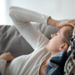 Upset depressed young woman lying on couch feeling strong headache